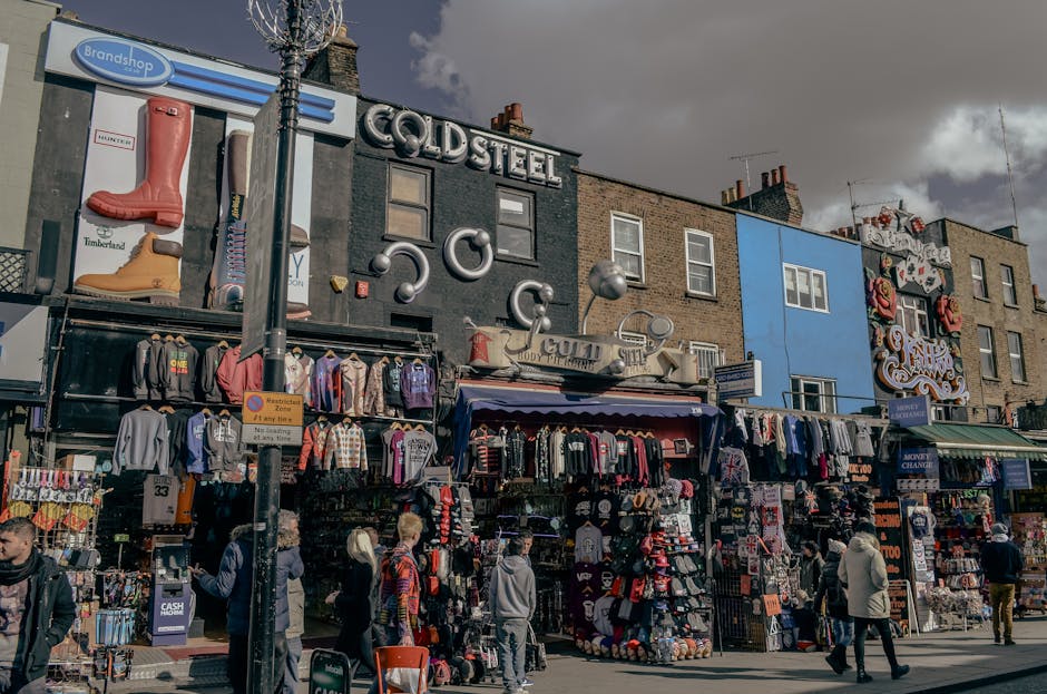 The exterior of a historic multi-story building with a light-colored facade featuring decorative architectural details, located on Hammersmith Broadway. Large red illuminated signs display words such 