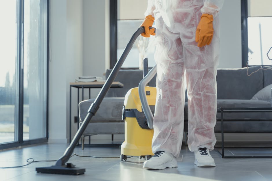 An indoor space near a window with natural light illuminating a cluttered area, featuring a small wooden table topped with tools and materials for deep cleaning projects. The floor appears dusty with 